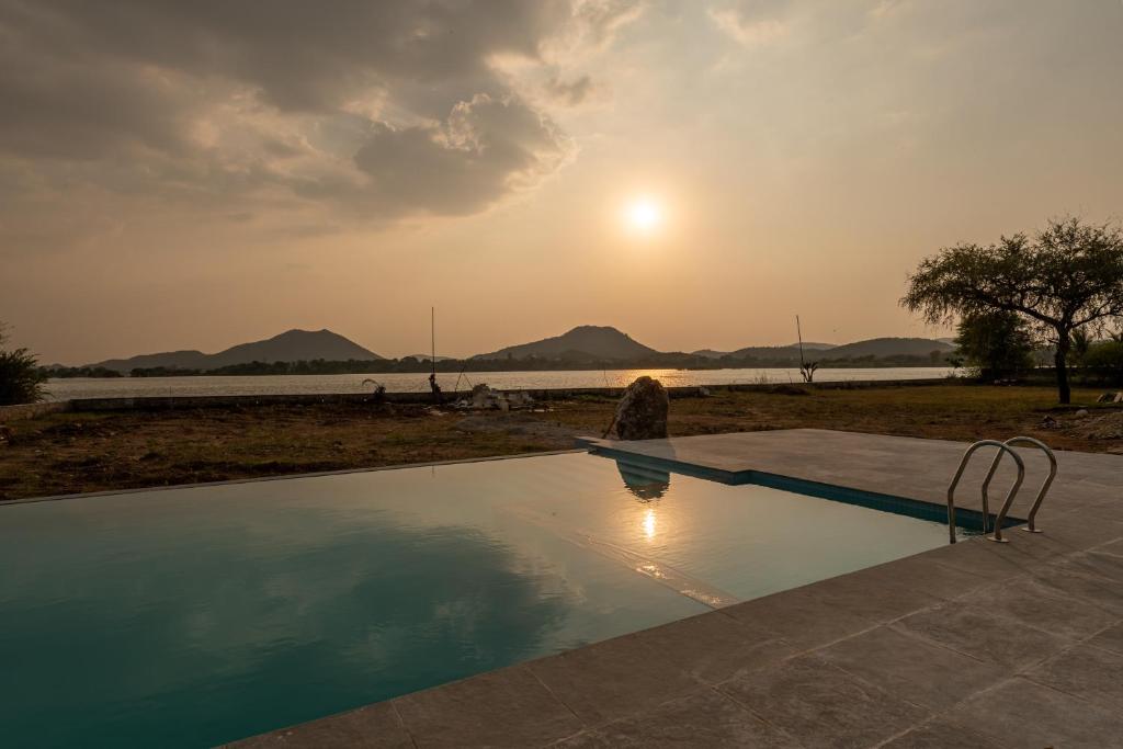 a swimming pool with the sunset in the background at 1br Cottage with Pool - Lake's End by Roamhome in Udaipur