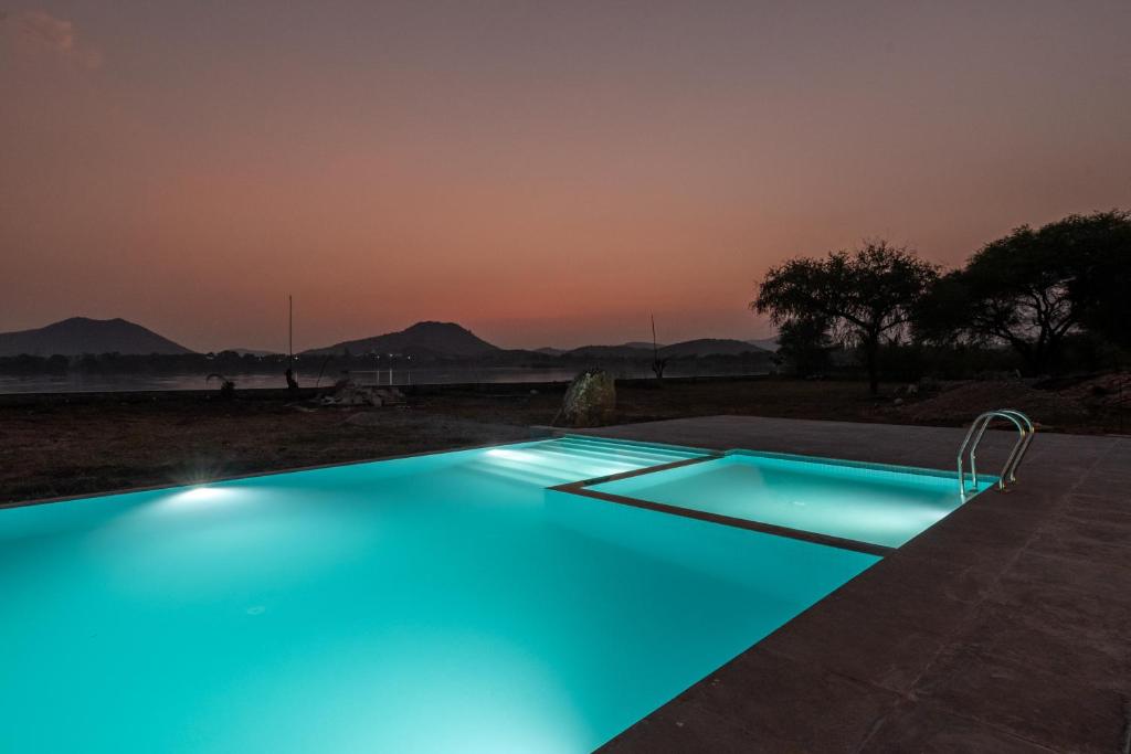 烏代浦的住宿－1br Cottage with Pool - Lake Escape by Roamhome，夜间拥有蓝色灯光的游泳池