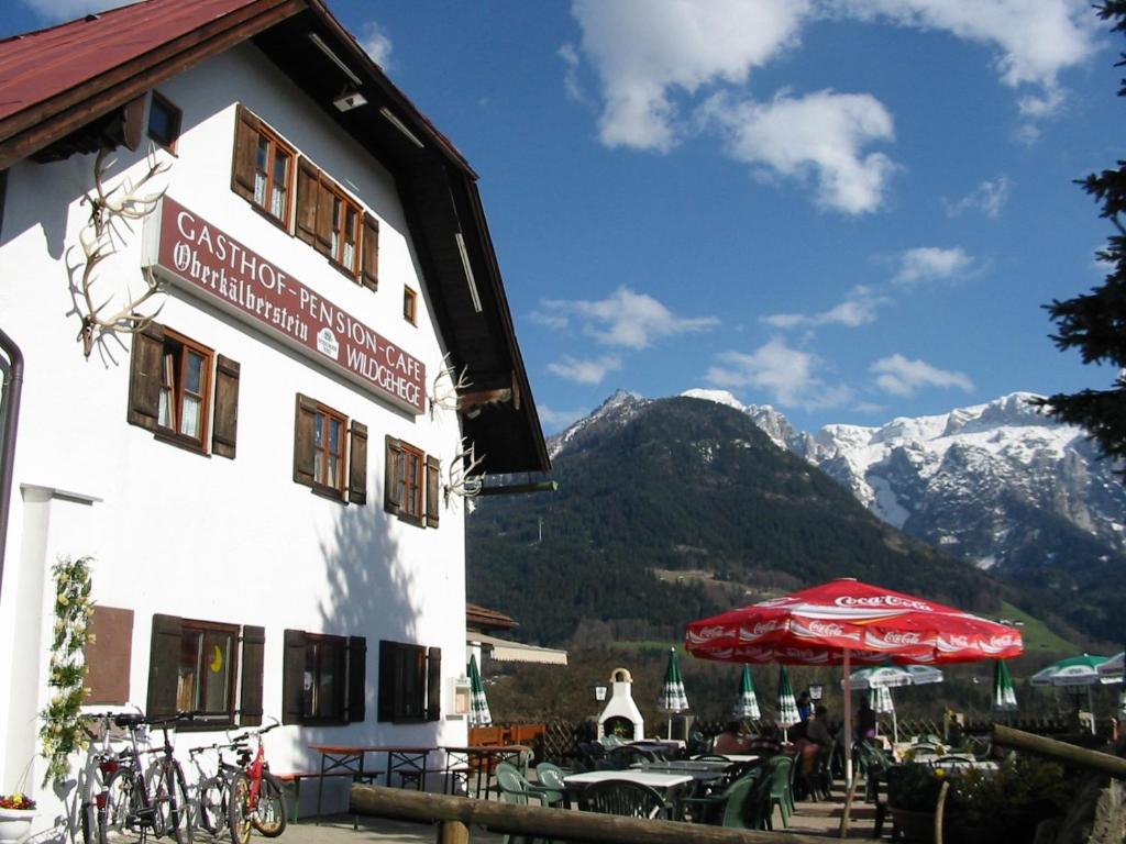 ein Hotel mit Tischen, Sonnenschirm und Bergen in der Unterkunft Berggasthof Oberkälberstein in Berchtesgaden