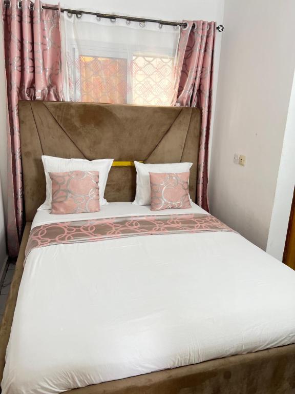 a bed with pink and white pillows on it at Chambre moderne avec cuisine à Bonamoussadi (Kotto) in Douala