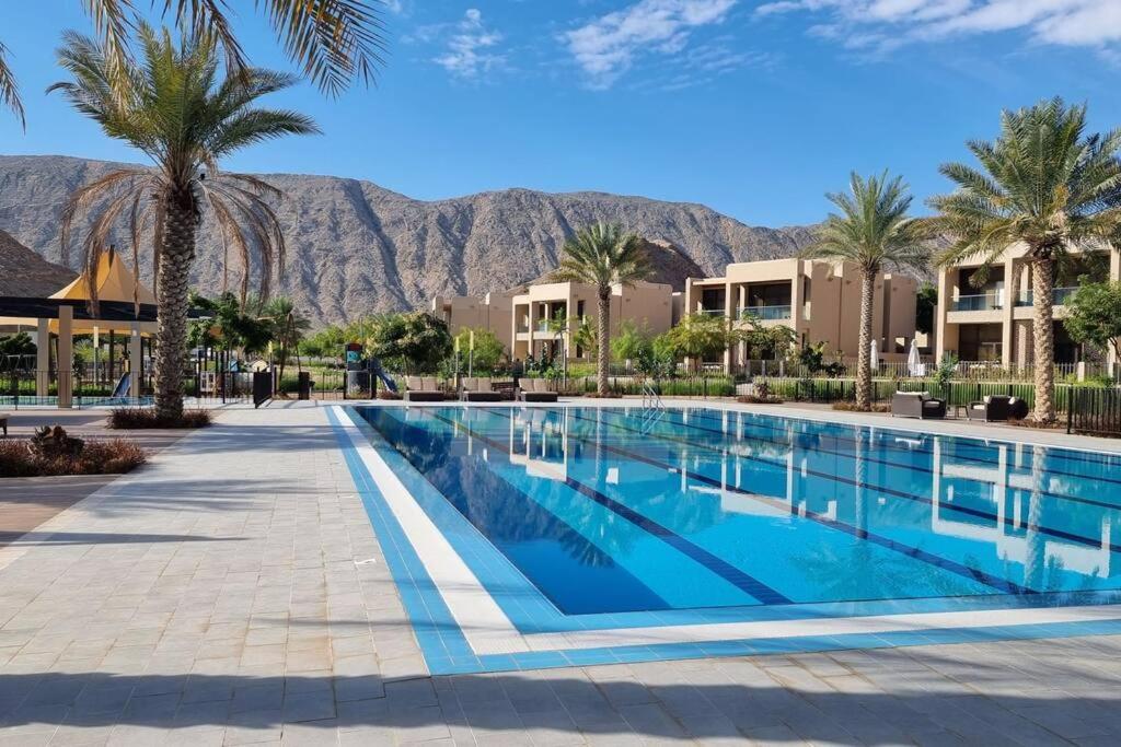 One Bedroom Apartment Muscat Bay في مسقط: مسبح فيه نخيل وجبال في الخلف