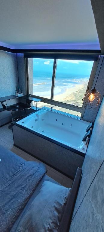 bañera grande en una habitación con ventana grande en מלון כרמל/מגדל C en Netanya