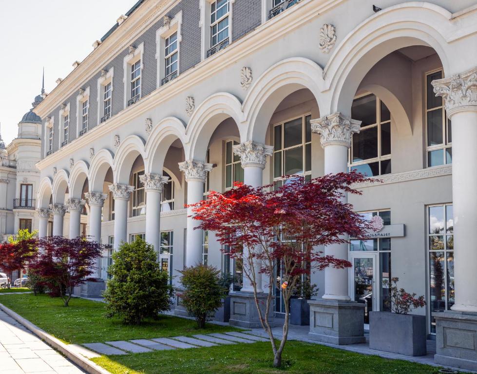 un edificio con columnas y un árbol rojo delante de él en Le Port Boutique Apart Hotel, en Batumi