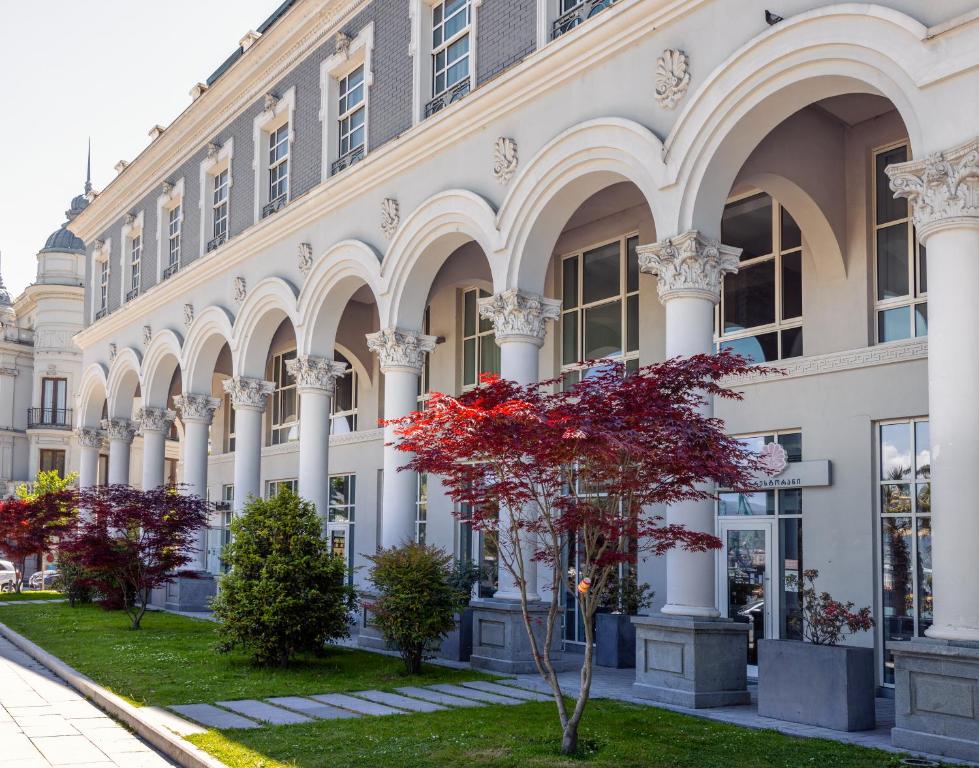 a building with columns and a red tree in front of it at Le Port Boutique Apart Hotel in Batumi