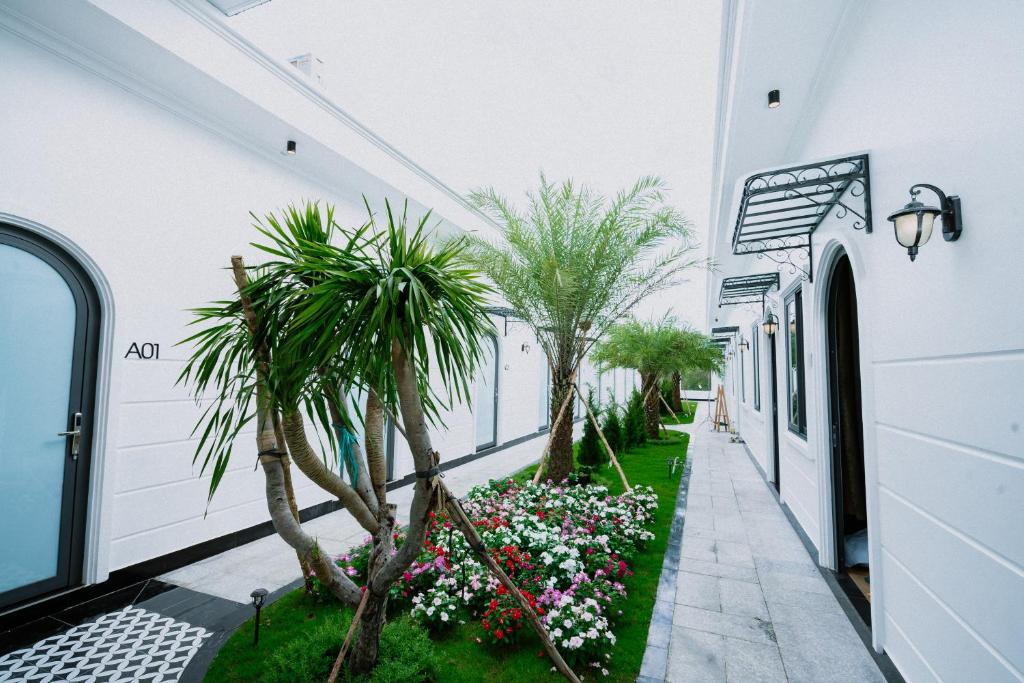 VÂN TRANG GARDEN HOTEL 2 في فينه لونج: ممر مبنى ابيض فيه اشجار النخيل والزهور