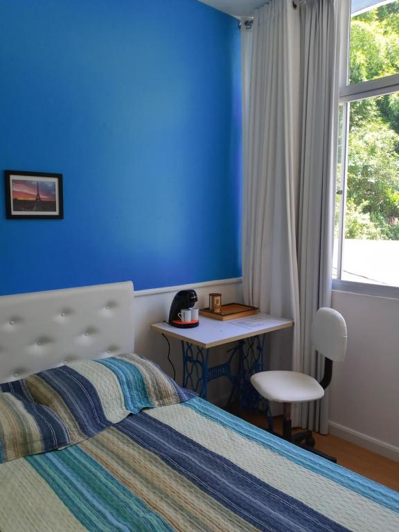 a blue room with a bed and a desk and a window at Quarto Acolhedor in Salvador