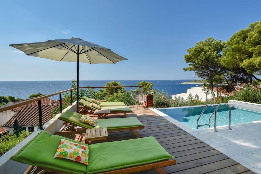 a deck with chairs and an umbrella next to a swimming pool at 4 bedrooms villa Hvar located 100m from the sea and 1,5 km from Hvar old town in Hvar