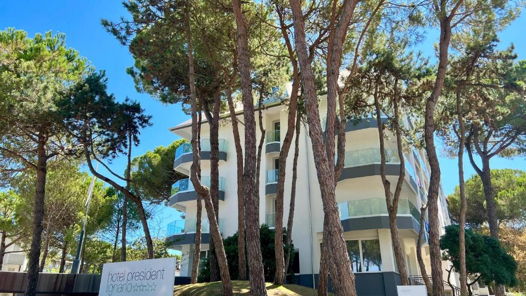 a white building with trees in front of it at Hotel President in Lignano Sabbiadoro