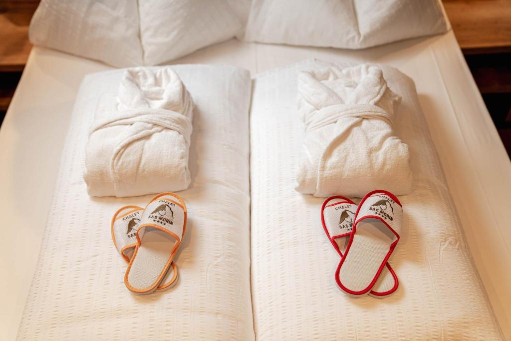 a bed with two towels and two pairs of slippers at Hotel Chalet Sas Morin in Pozza di Fassa