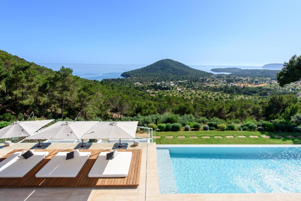a pool with lounge chairs and umbrellas next to a mountain at Sa Caleta Hill in Sant Josep
