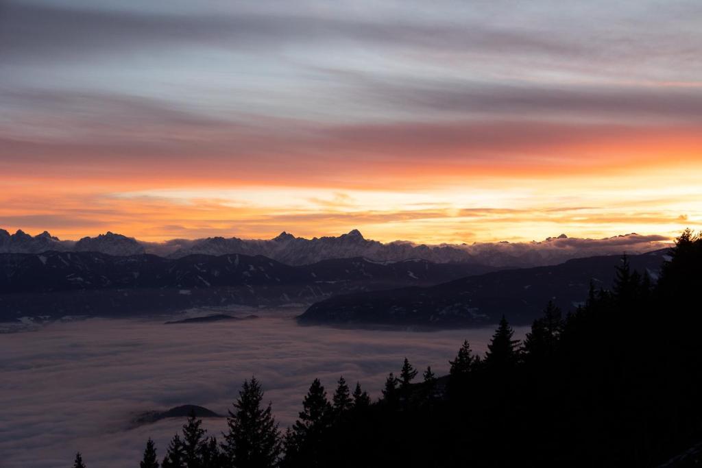 um pôr-do-sol sobre as montanhas com uma camada de nuvens em L&P Appartement Gerlitzen & Pool - Haus Enzian em Kanzelhöhe