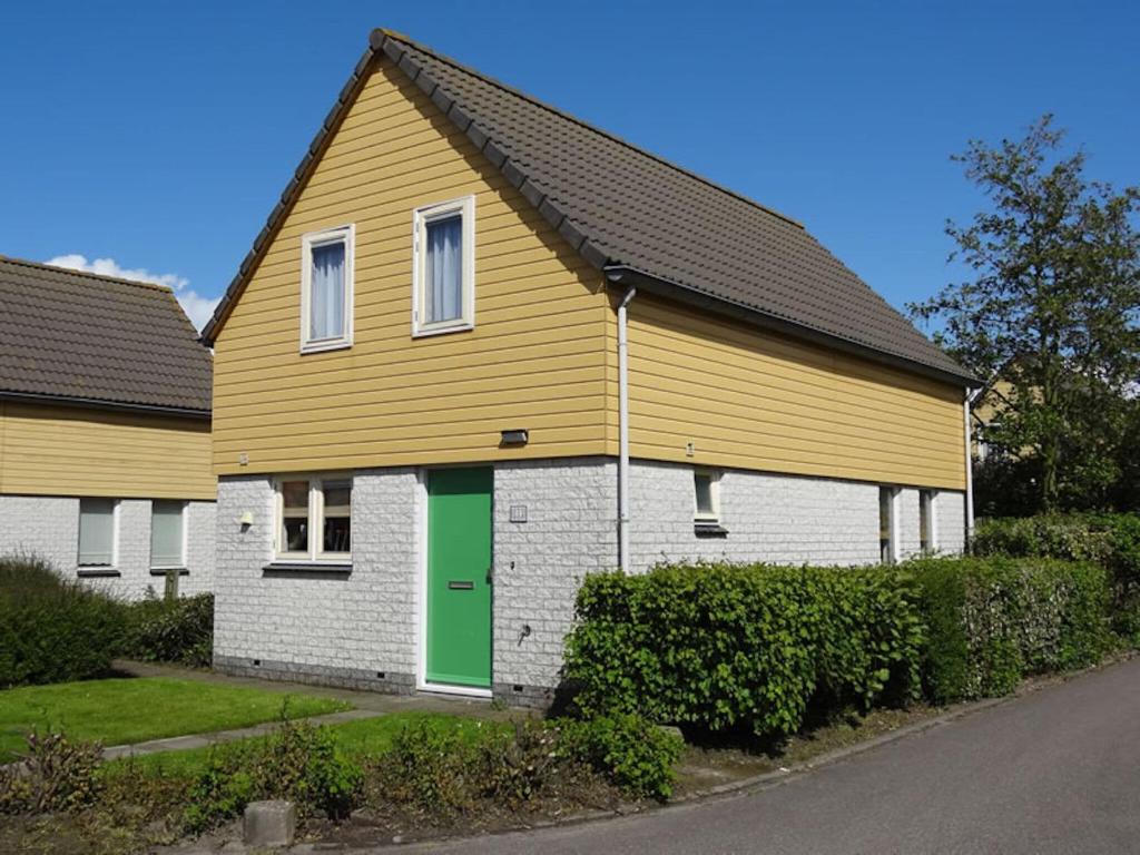 a yellow and white house with a green door at Nice holiday home with sauna, in a holiday park only 200m away from the beach in Wemeldinge