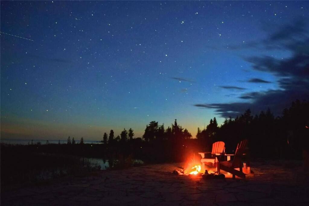a campfire with a table and a chair at night at **WATERFRONT**BEAUTIFUL MODERN TOBERMORY COTTAGE in Miller Lake