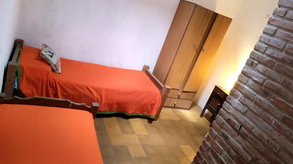 Habitación con cama con manta naranja y pared de ladrillo en Alquiler Temporario en Villa Cura Brochero