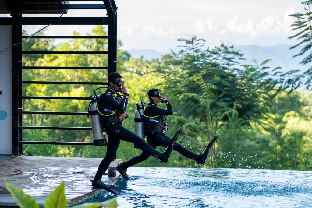 zwei Personen in Neoprenanzügen, die im Wasser laufen in der Unterkunft Deep Roots Dive & Yoga Resort in Nusa Penida