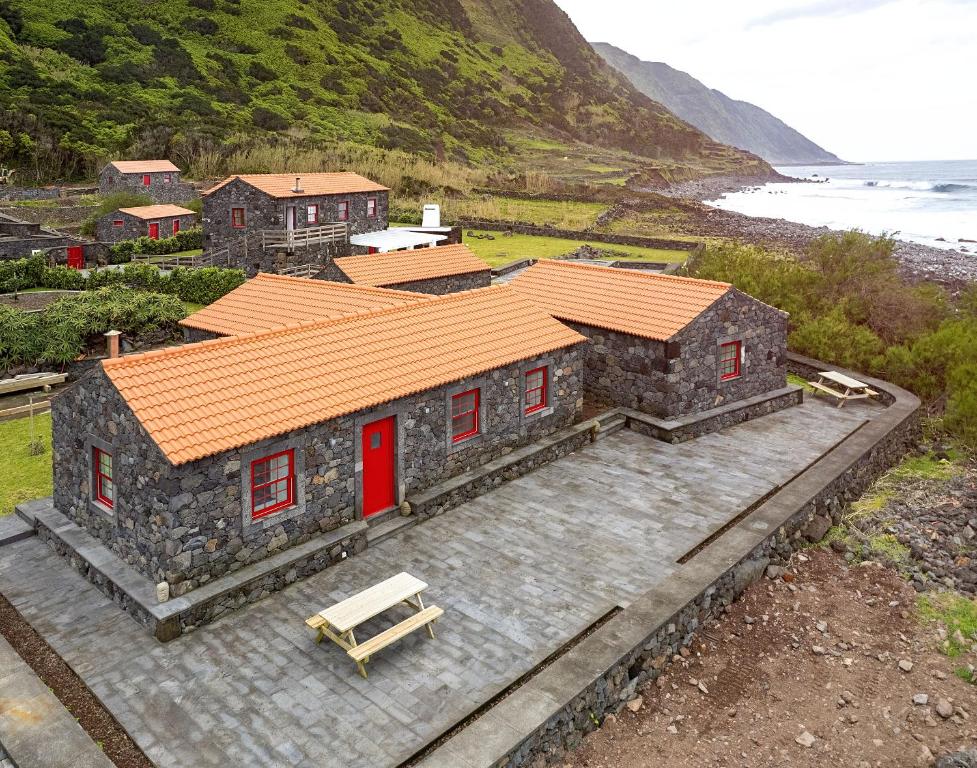 une maison en pierre avec des portes rouges et un banc dans l'établissement Kuanza Nature Experience, Fajã do Belo, à Fajã da Caldeira de Santo Cristo