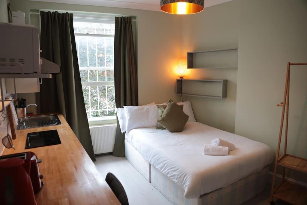 een kleine kamer met een bed, een bureau en een raam bij Cosy Chic Studio in King's Cross in Londen