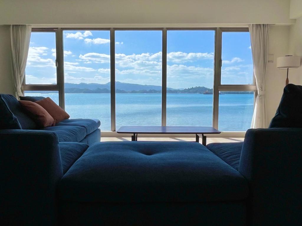 una sala de estar con 2 sofás azules y vistas al océano. en Lala court seaside Yagaji / Vacation STAY 3226, en Nago
