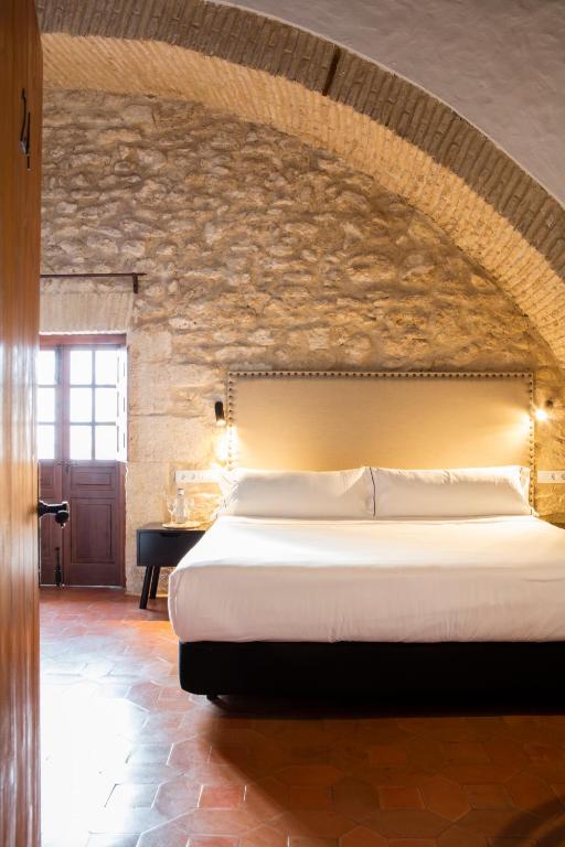 a bedroom with a large bed with a stone wall at Hotel Tugasa Convento San Francisco in Vejer de la Frontera