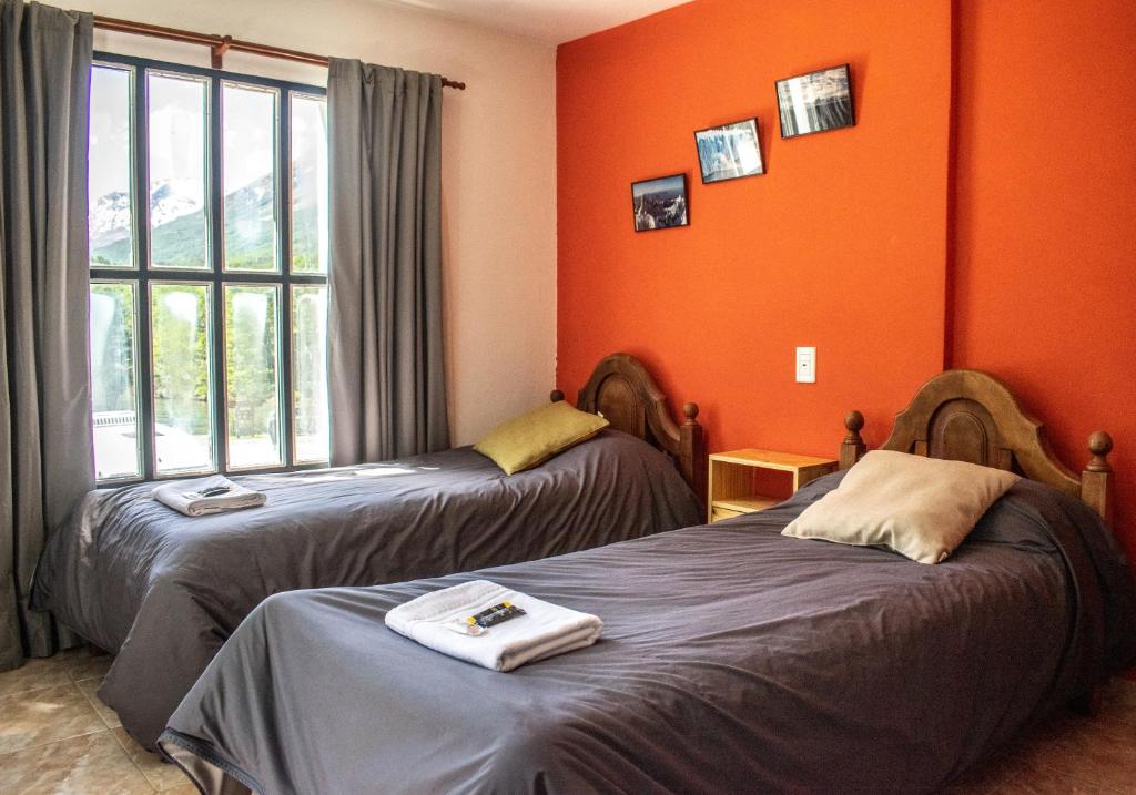 2 camas en una habitación con paredes de color naranja en Hostería Punta Sur en Lago del Desierto en El Chaltén