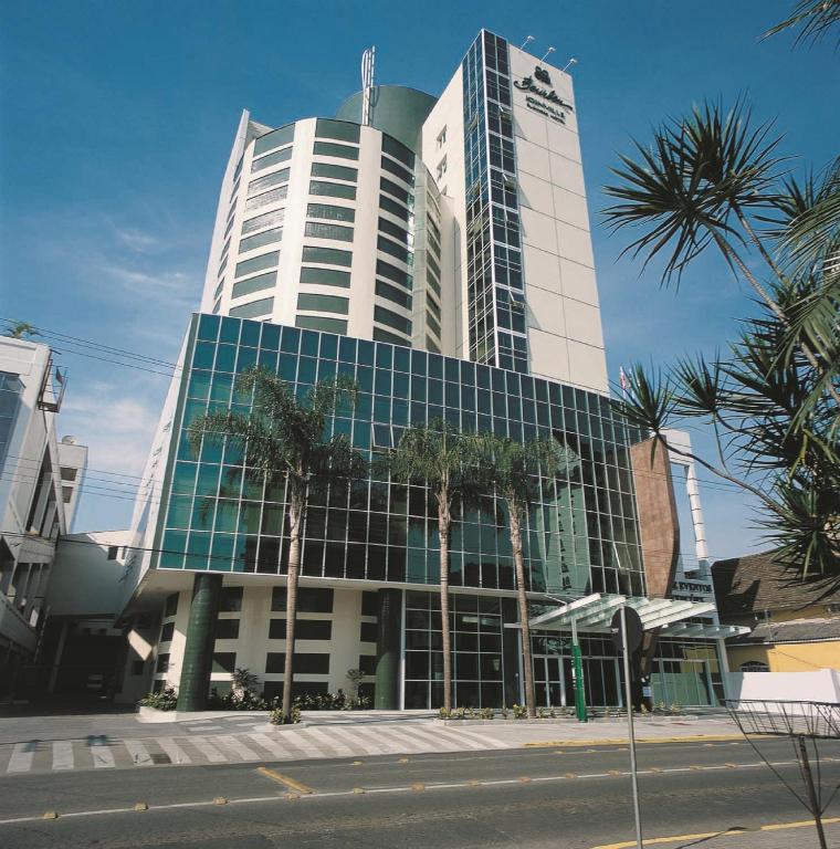 Un edificio alto con palmeras delante. en Bourbon Convention Hotel Joinville, en Joinville