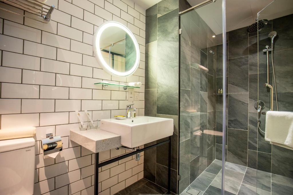 A modern bathroom with a wall-mounted sink, lit mirror, toilet, and glass shower.