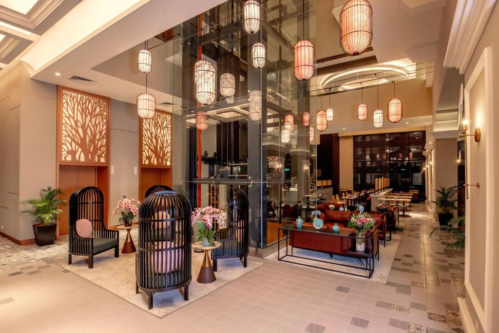 A bright lobby seating area features sculptural black chairs, plants, and a glass lift.