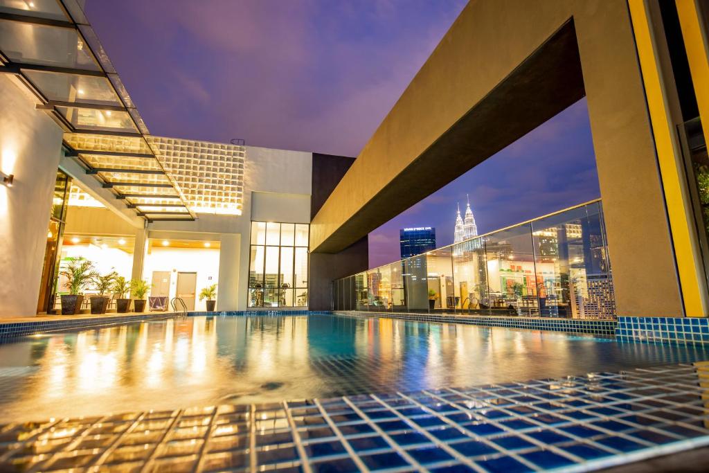 A rooftop pool reflects evening lights with a city skyline beyond the glass railing.