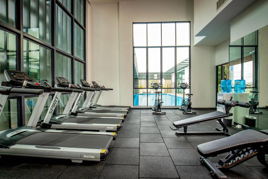 A bright hotel gym with treadmills, bikes, benches, and a pool view.