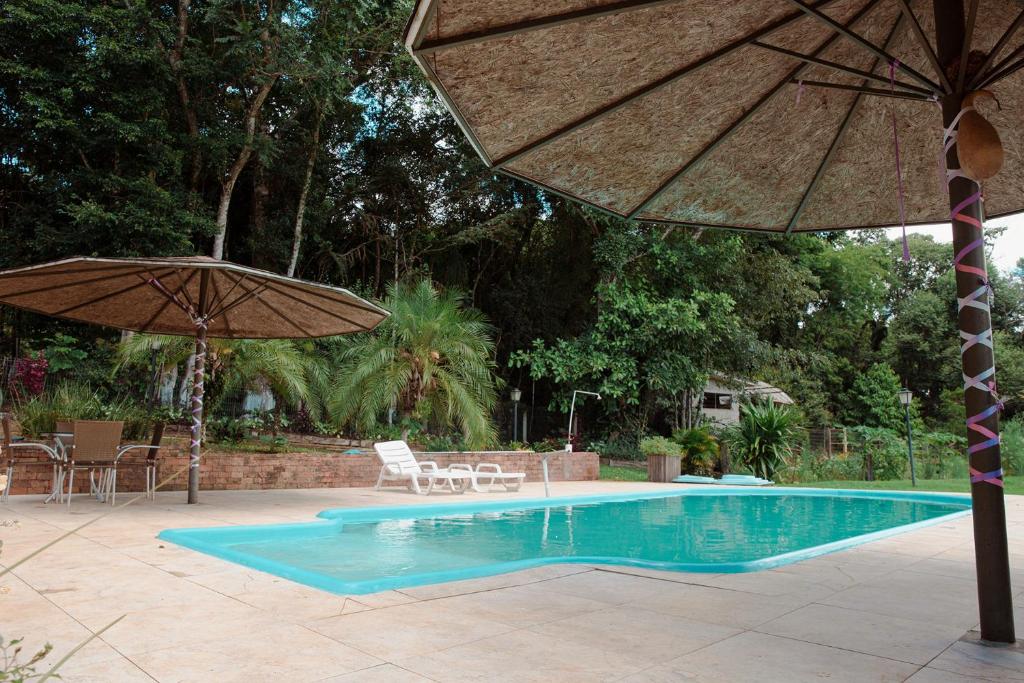 uma piscina com um guarda-sol, uma mesa e cadeiras em Casa de Campo com Piscina e lazer em Cascavel PR em Cascavel