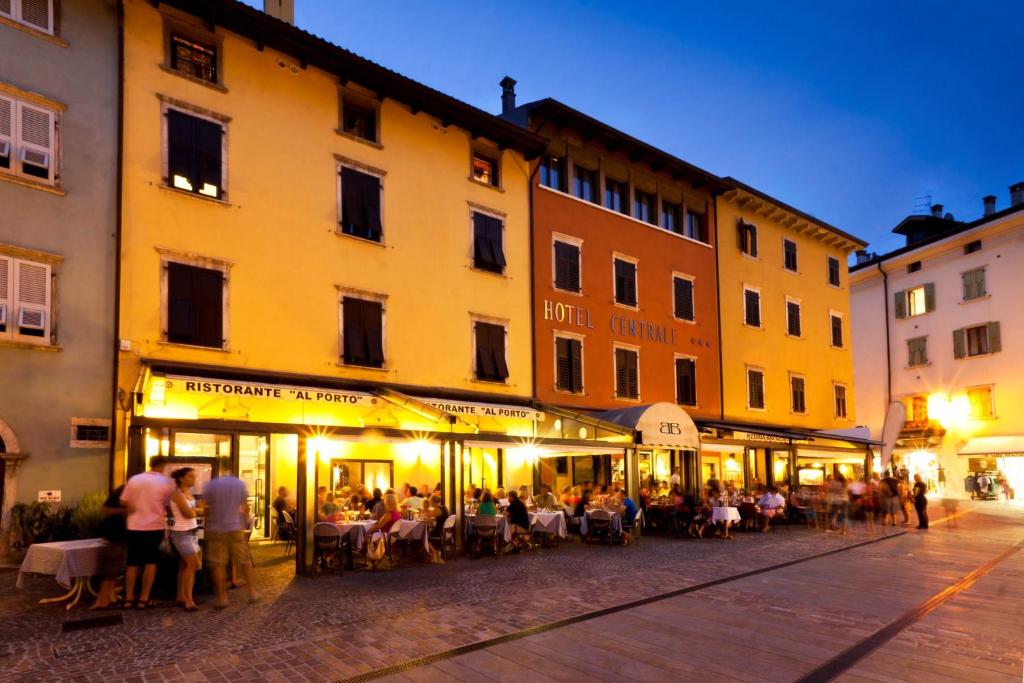 un groupe de personnes assis à des tables à l'extérieur d'un bâtiment dans l'établissement Hotel Centrale, à Nago-Torbole