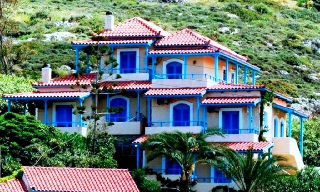 a large house with blue windows and a mountain at Corina Apartments in Sitia