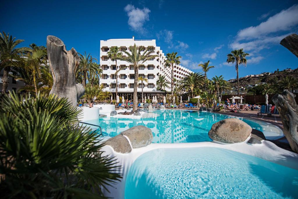 a pool at a resort with palm trees and a building at Corallium Beach by Lopesan Hotels - Adults Only in San Agustin