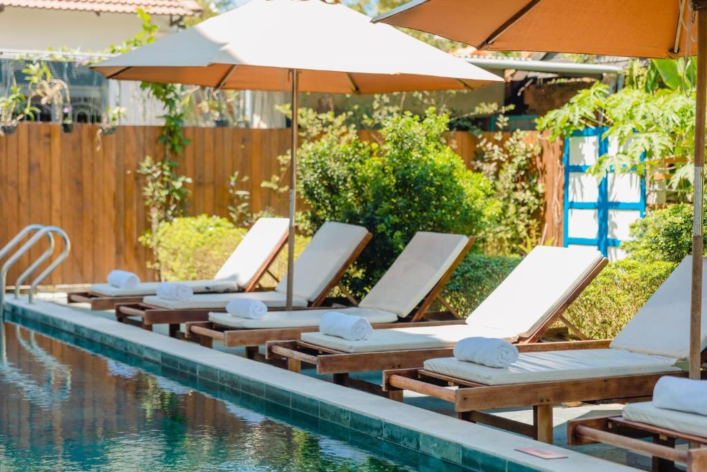uma fila de espreguiçadeiras e um guarda-sol junto a uma piscina em The Sunshine Hoi An Villa em Hoi An
