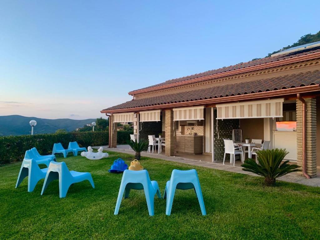 un groupe de chaises bleues assises dans l'herbe à côté d'une maison dans l'établissement Miramare Castellabate, à Santa Maria di Castellabate