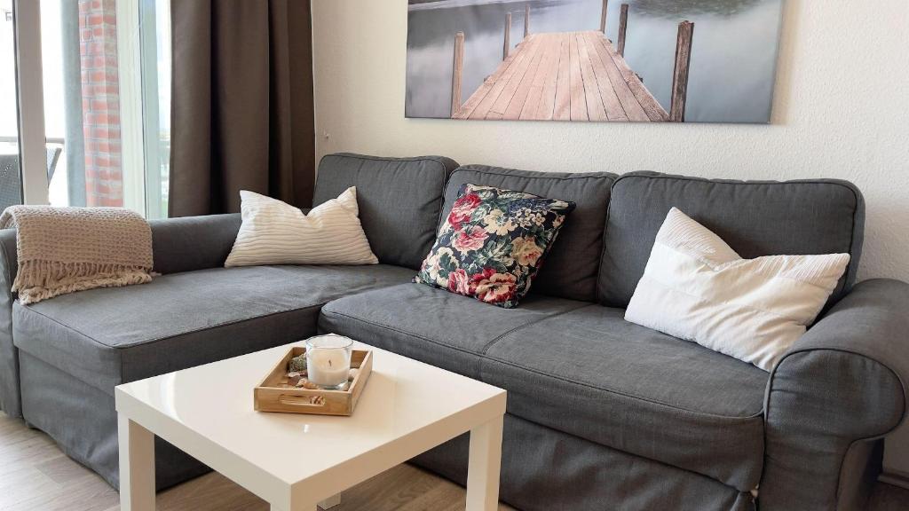 ein Wohnzimmer mit einem grauen Sofa und einem weißen Tisch in der Unterkunft Strandhaus Nordseebrandung Fewo A2.4 in Cuxhaven