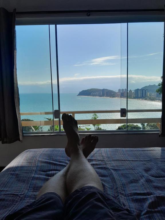 una persona sdraiata su un letto con i piedi su una finestra di Por de sol no mar da cama a Caraguatatuba