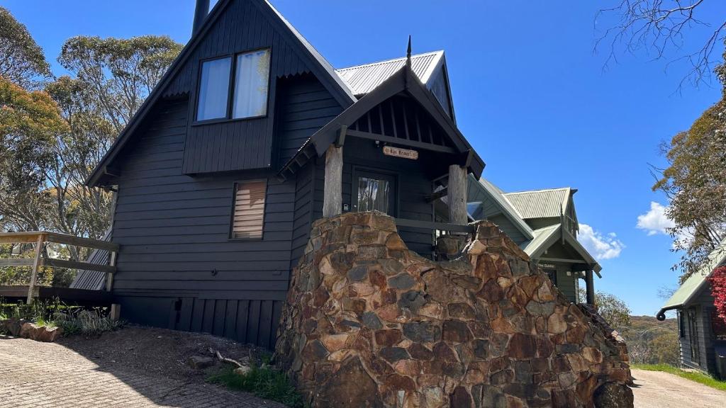 a black house with a stone wall in front of it at Alps Heimers in Dinner Plain