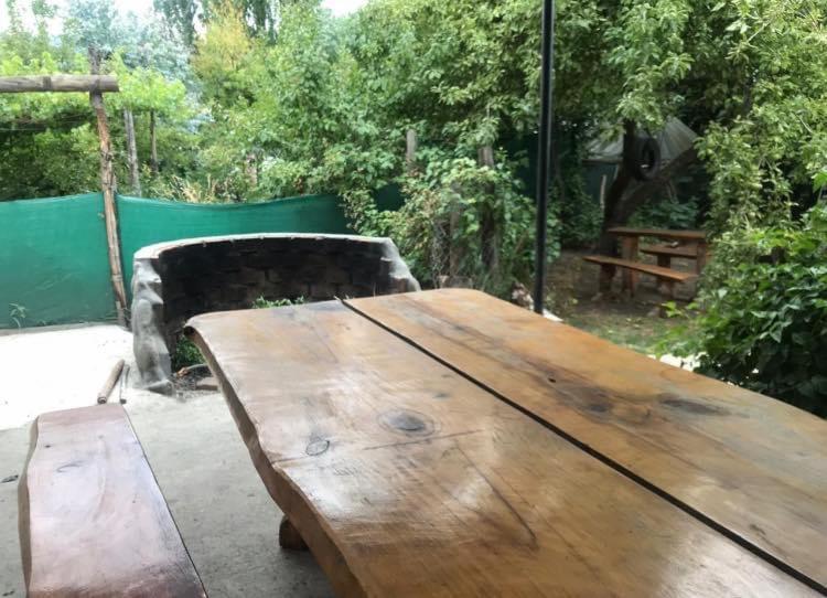una mesa de madera en un jardín con un banco en Cabaña familiar en pleno centro de Bolsón para 5-6 personas en El Bolsón