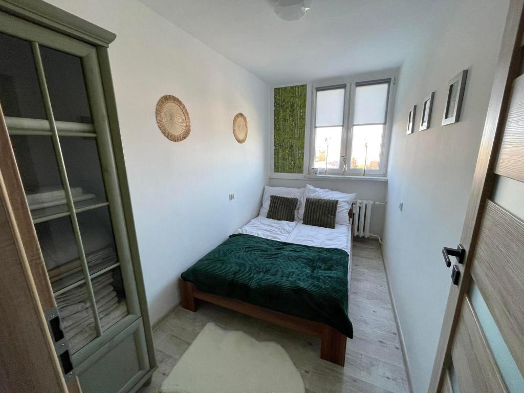 een kleine slaapkamer met een bed met een groene deken bij Apartament Arverso in Bolesławiec