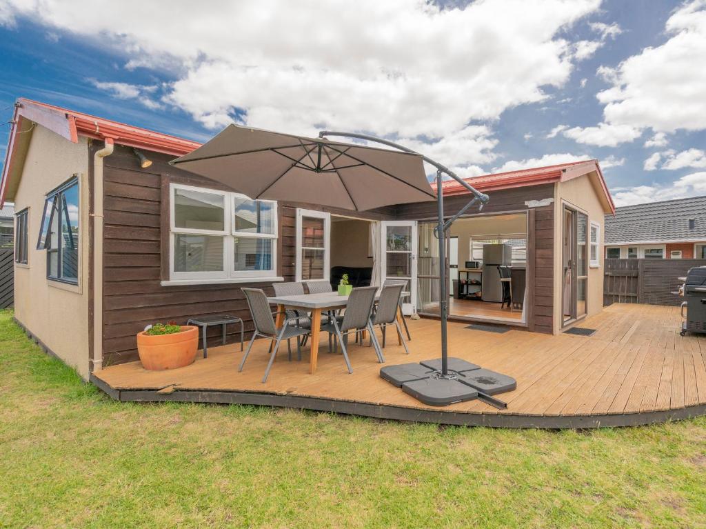 eine Terrasse mit einem Tisch und einem Sonnenschirm in der Unterkunft Beach House on Hetherington - Whangamata Home in Whangamata