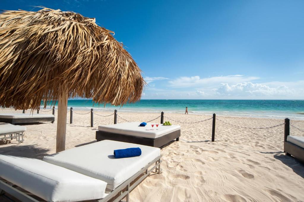 einen Strand mit zwei Liegestühlen und einem Strohschirm in der Unterkunft Grand Bavaro Princess - All Inclusive in Punta Cana