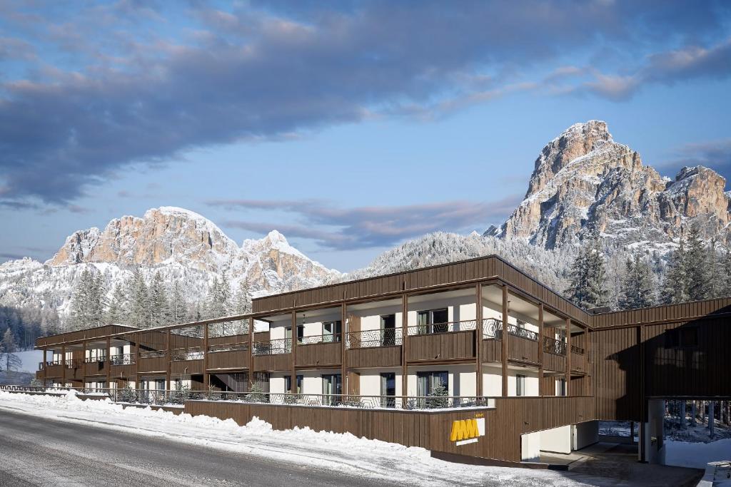 a building with a snow covered mountain in the background at Movi Family Apart-Hotel ****s in Corvara in Badia