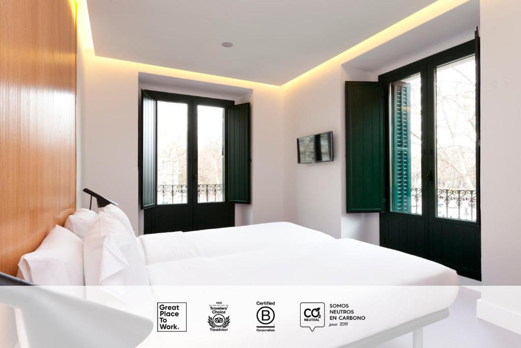 um quarto com uma cama branca e 2 janelas em SLEEP'N Atocha - B Corp Certified em Madrid