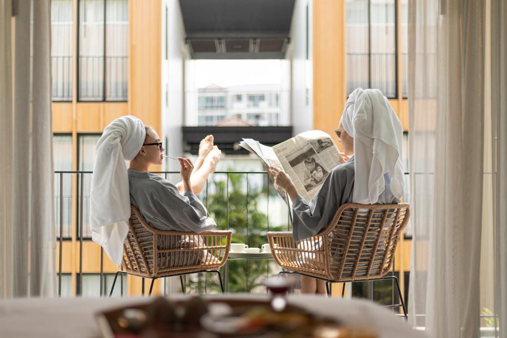 Dos personas sentadas en sillas leyendo un periódico en un balcón en Craftsman Bangkok, en Bangkok