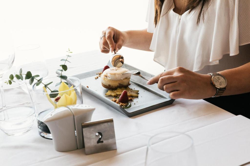 A guest prepares a plated dessert at a white-tablecloth dining table.