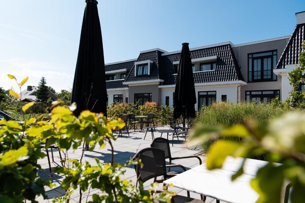 eine Gruppe von Sonnenschirmen, Tischen und Stühlen vor einem Gebäude in der Unterkunft Boutique Hotel ter Zand in Burgh Haamstede