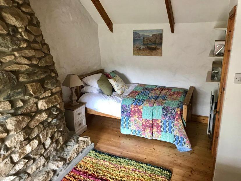 um quarto com uma cama e uma parede de pedra em Dog friendly cottage with woodland & lake em Helston