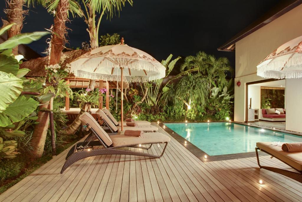 a deck with chairs and an umbrella and a swimming pool at Elok Villas in Seminyak