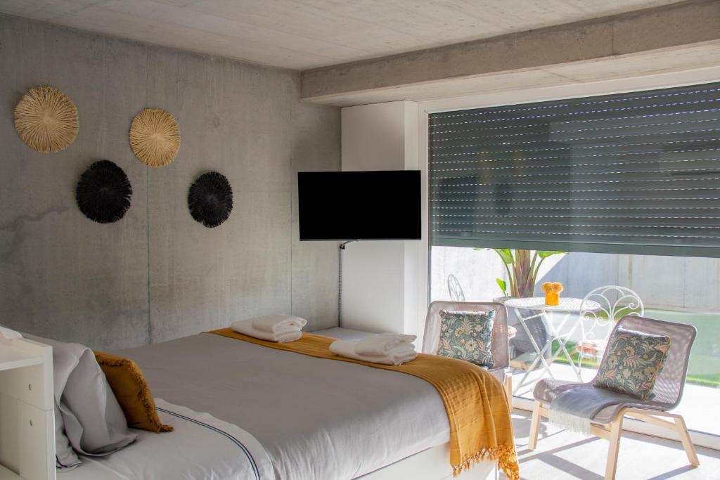 ein Schlafzimmer mit einem Bett und zwei Stühlen und einem Fernseher in der Unterkunft Casa das Falcoeiras - Estúdio com terraço privado in Aveiro